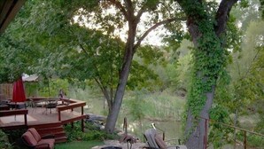 An outdoor patio area with stone flooring, a wooden deck, and seating arrangements including chairs and a table. - Sedona Creekfront Hideaway ~ a beautiful private home on 2 acres of creek front  (Lake Montezuma)