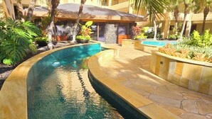 Une piscine en forme de courbe, bordée de pierres, entourée de plantes tropicales et adossée à un bâtiment sur lequel on peut lire l’inscription « The Polo Beach Club ».