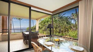 Un coin repas avec une table en verre, des chaises et une vue sur les palmiers et l’océan.