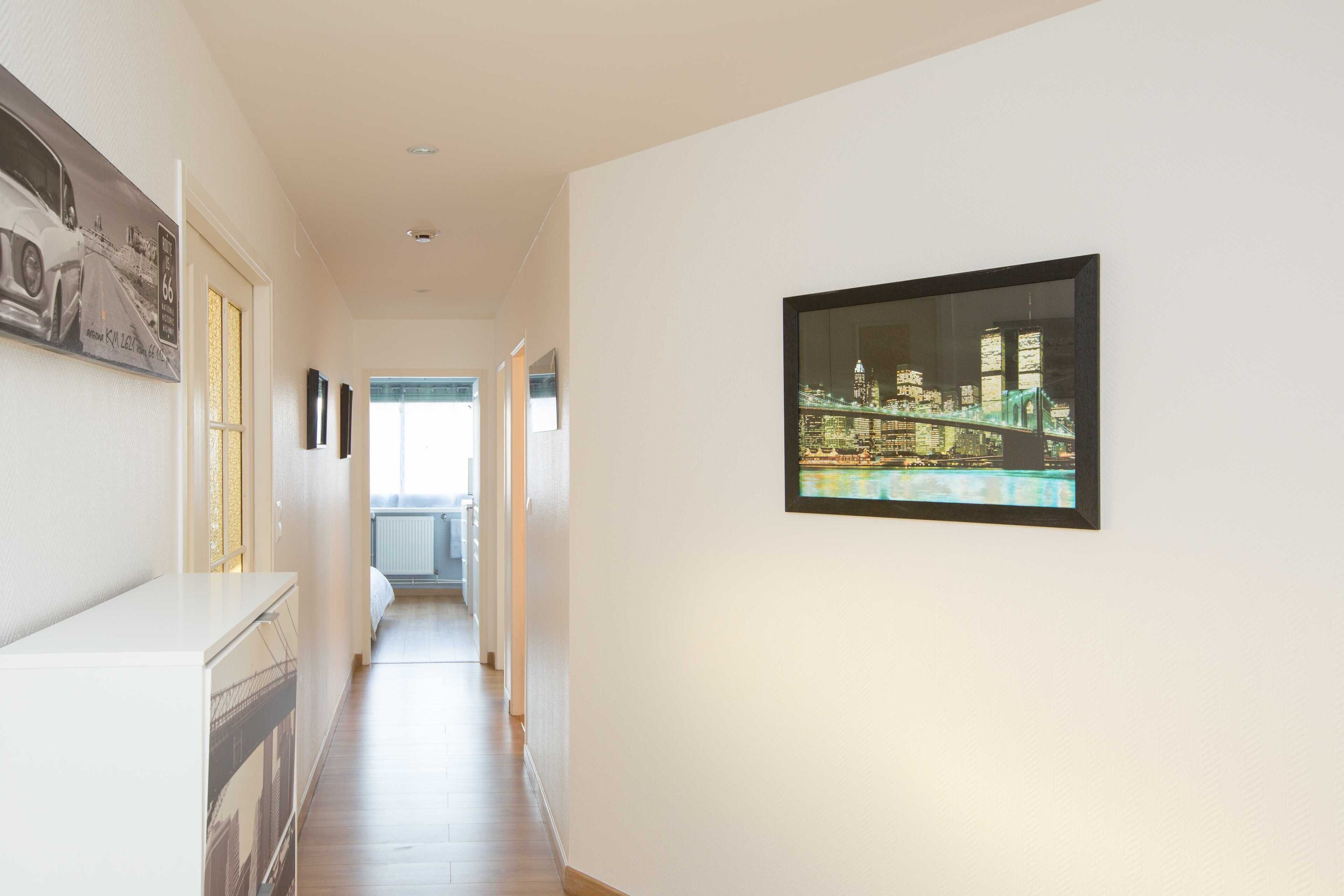 Een gang met een stadsgezichtschilderij aan de muur, een witte console tafel en een doorkijk naar een andere kamer.