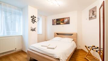 A neatly arranged bedroom with a wooden bed, a radiator, a window with sheer curtains, and a wall-mounted artwork.