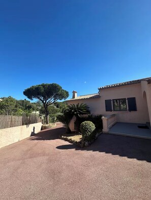 Uma casa com entrada por um caminho pavimentado, uma árvore grande e um pequeno jardim.