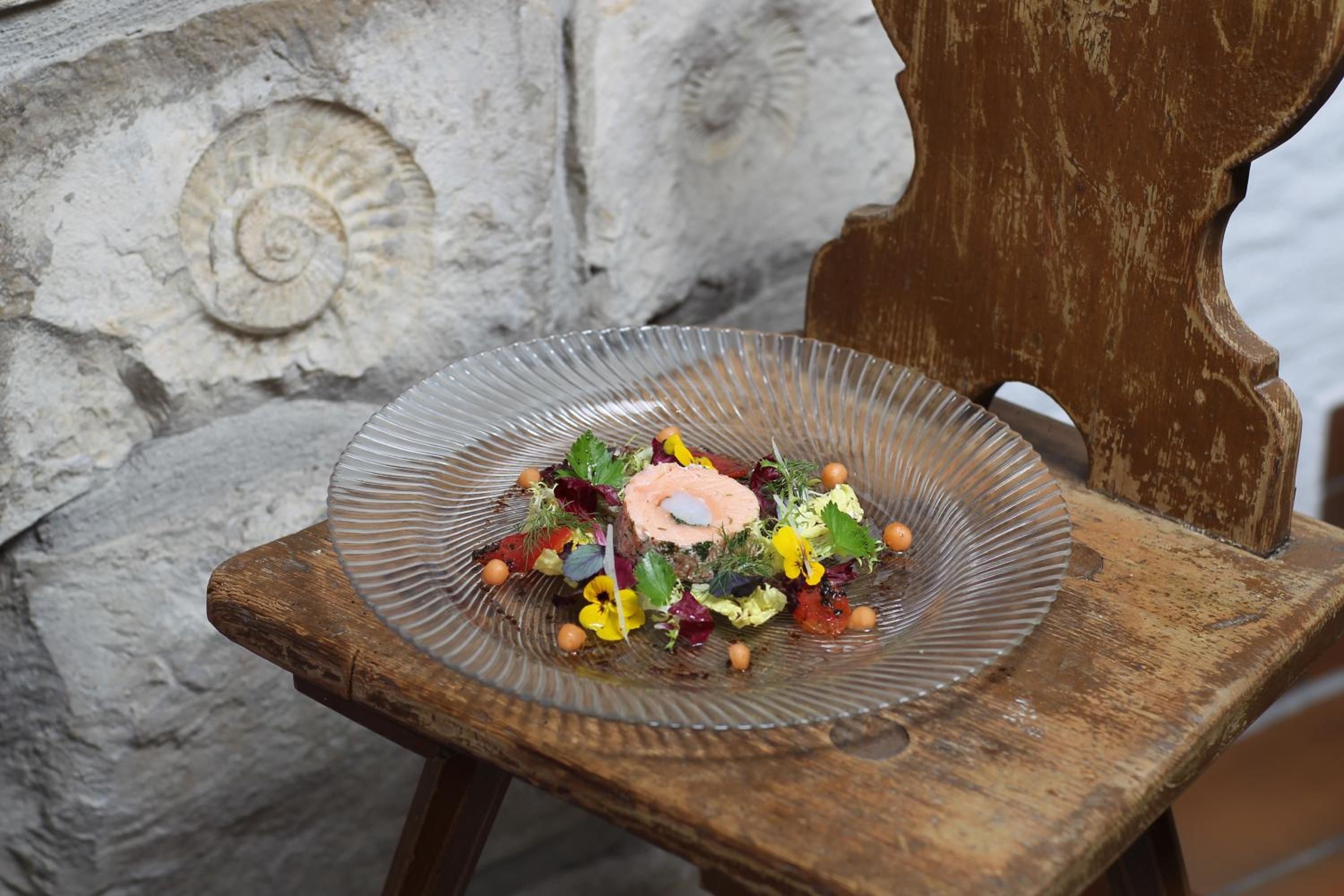 A plate of food on a rustic wooden chair with a stone wall in the background.