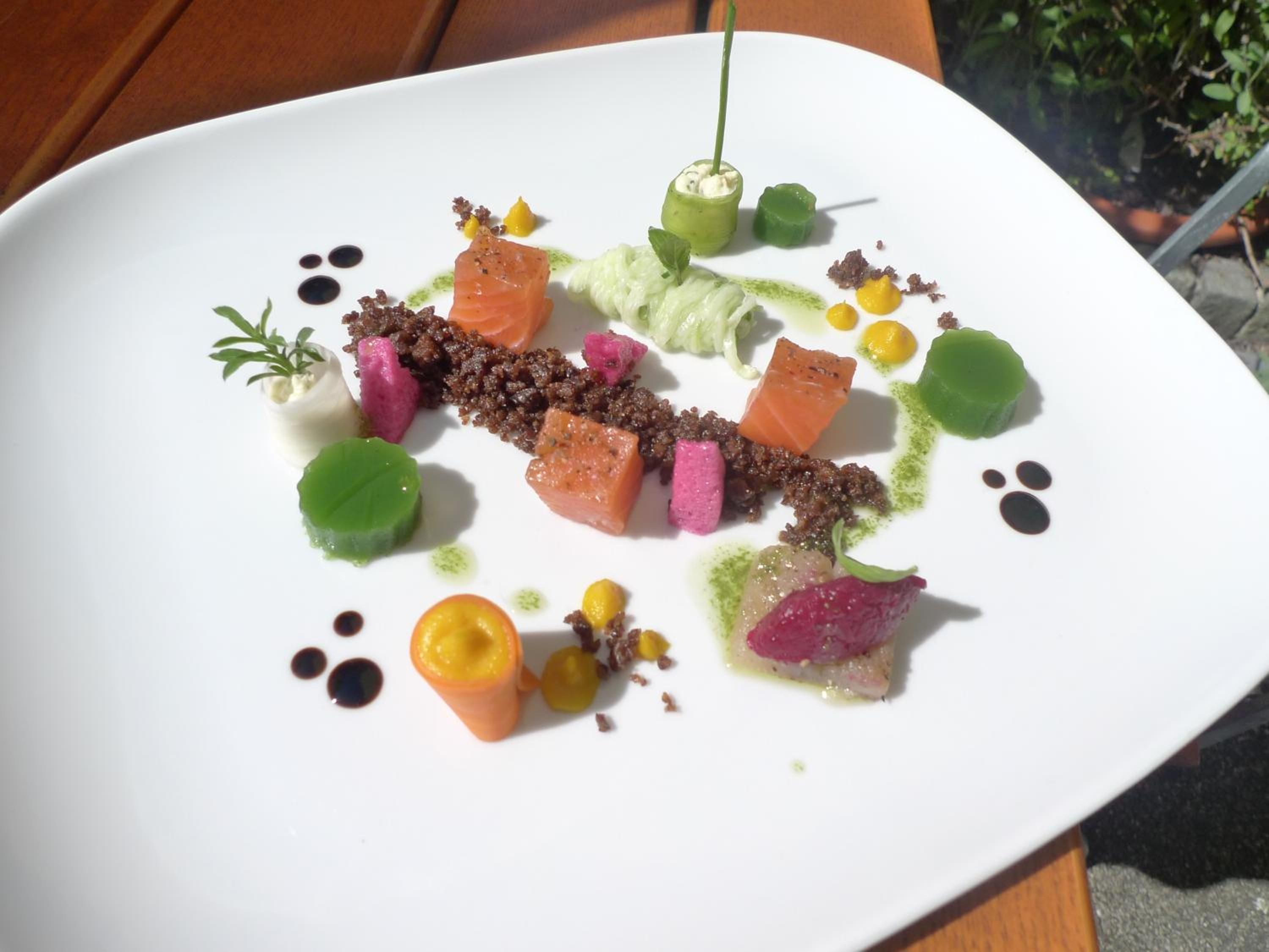 Une assiette blanche contenant divers aliments, notamment du saumon, des légumes et des sauces.