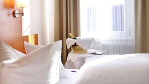 Een hotelkamer met een opgemaakt bed, een nachtkastje met fles en glazen, en een raam met gordijnen.