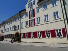 Un edificio de varios pisos con contraventanas rojas, una entrada visible y un cartel.