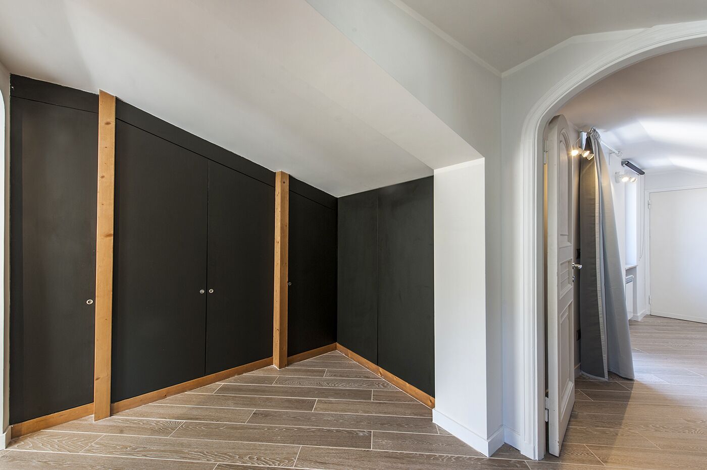 A hallway with dark-colored wardrobes and wooden beams, leading to a room with a tiled floor.