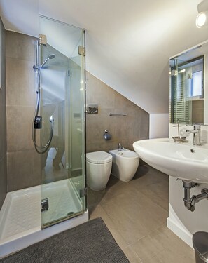 A modern bathroom with a glass-enclosed shower, a freestanding toilet, a bidet, and a sink with a mirror.