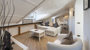 A modern loft bedroom with a sloped ceiling, a white sofa, a small coffee table, and a dining area with a white table and chairs.