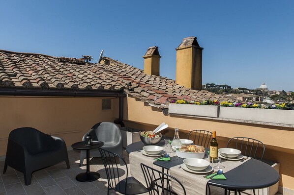 A rooftop terrace with a table set for dining, chairs, and a view of the cityscape.