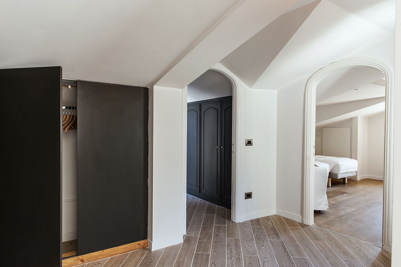 Un pasillo con un armario oscuro, una puerta blanca y un dormitorio con cama.