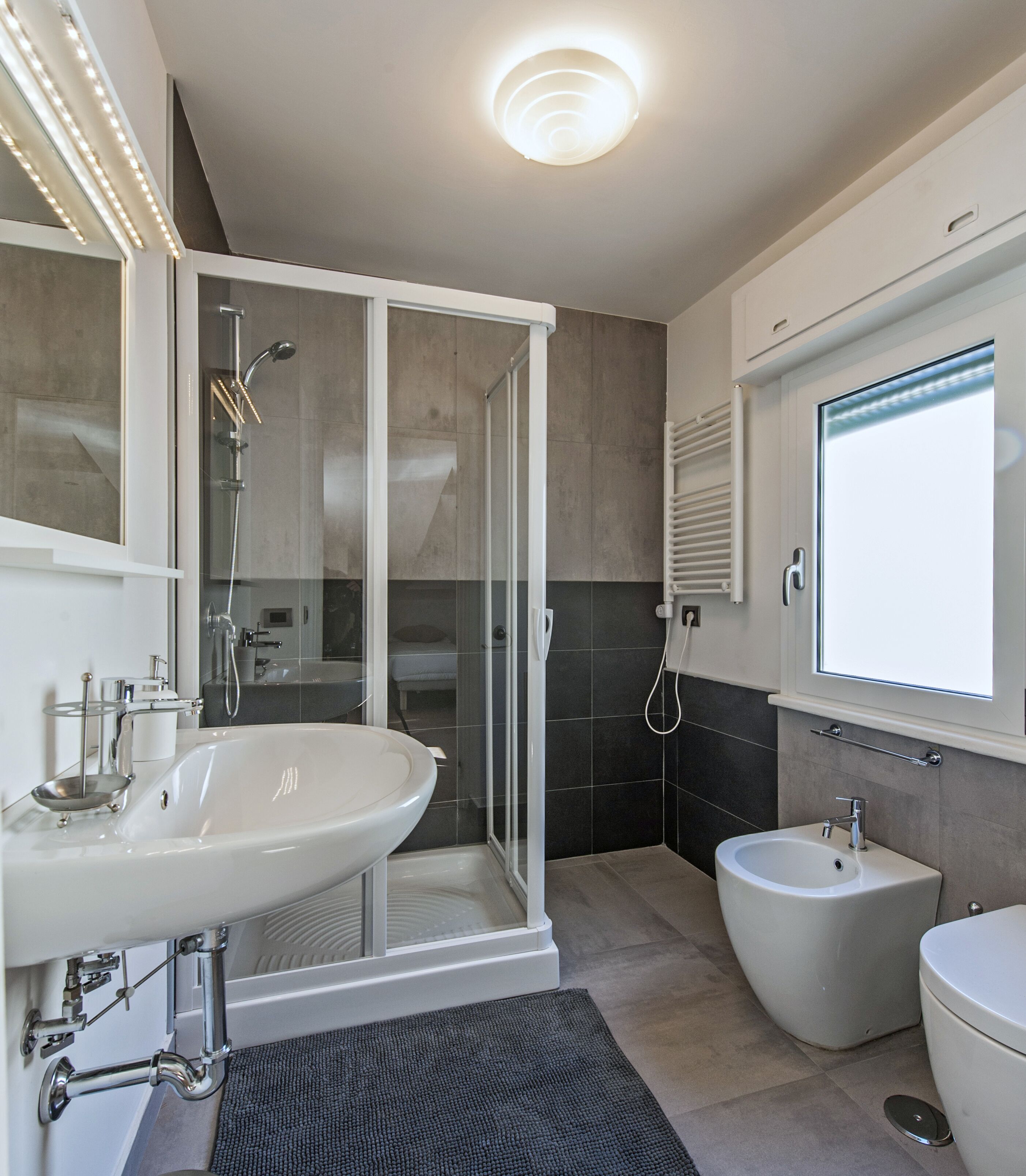 A modern bathroom with a glass-enclosed shower, a pedestal sink, a bidet, and a toilet.