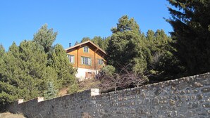 Un mur de pierre et une maison en bois avec un toit en pente, entourés d’arbres denses.