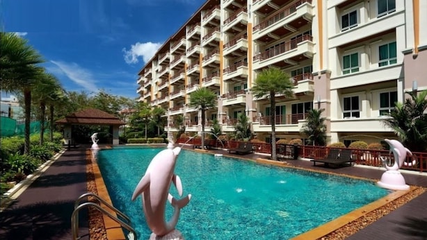 Um hotel com piscina, várias varandas e um jardim tropical.