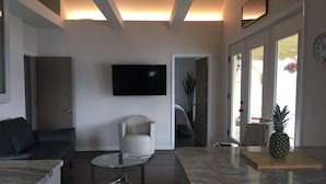 A modern living room with a sofa, a glass coffee table, a TV mounted on the wall, and a kitchen area with a marble countertop and a pineapple on it. - Waterfront Keuka Lake INCREDIBLE VIEWS • BOAT SLIP • TWO BALCONIES 3rd floor (Hammondsport)