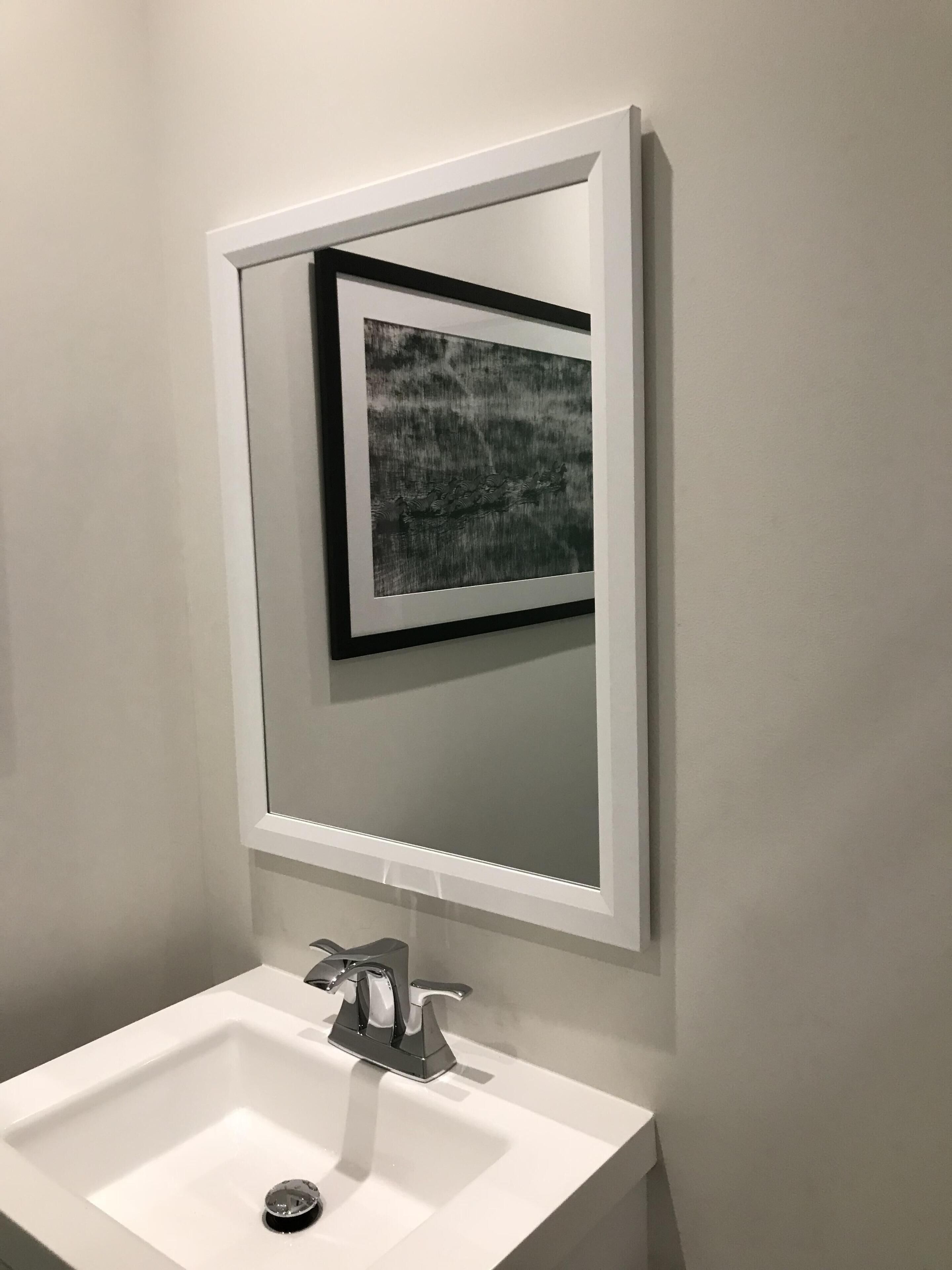 A bathroom with a white sink, a modern faucet, and a framed artwork above the mirror.