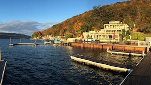 A lakeside dock with a wooden pier, a building with a balcony, and a mountainous backdrop. - Waterfront Keuka Lake INCREDIBLE VIEWS • BOAT SLIP • TWO BALCONIES 3rd floor (Hammondsport)