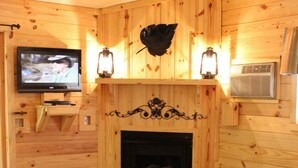 L’intérieur chaleureux d’un chalet avec un mur en bois, une cheminée, un téléviseur fixé au mur et un canapé.