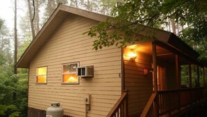 Une cabane dotée d’une terrasse en bois, d’un porche couvert et d’une petite dépendance attenante avec une fenêtre.