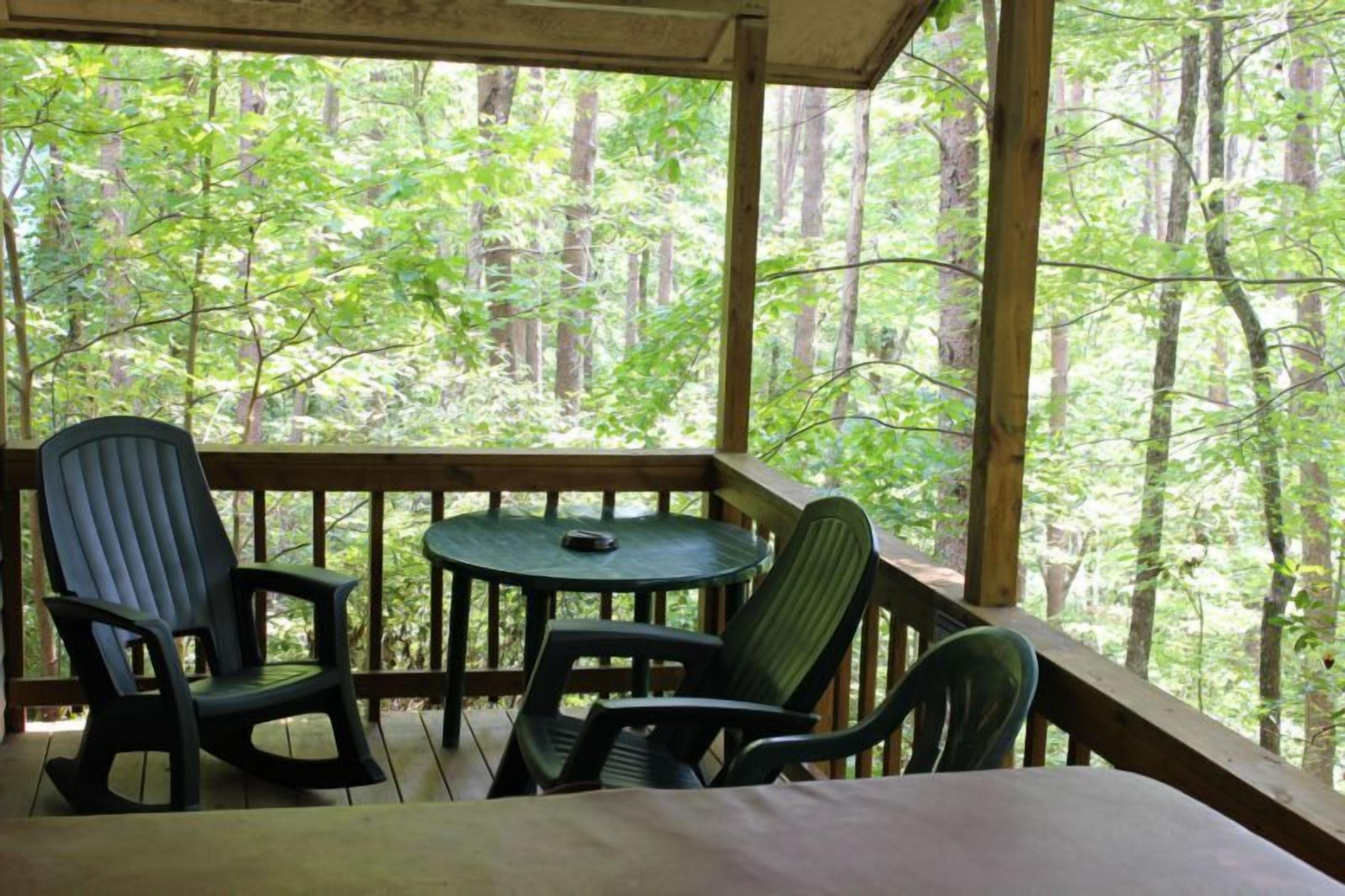 A wooden deck with a table and chairs, overlooking a forested area.