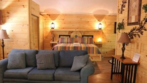 Une pièce chaleureuse avec un décor intérieur en bois, un lit avec une literie à rayures, un canapé bleu et deux lampes de chevet.