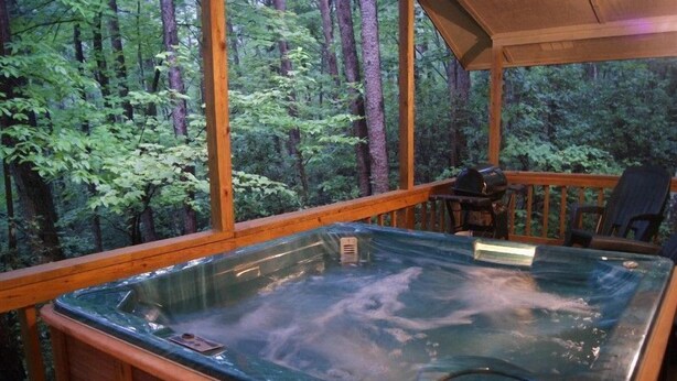 Un bain à remous installé sur une terrasse en bois, avec vue sur une forêt.