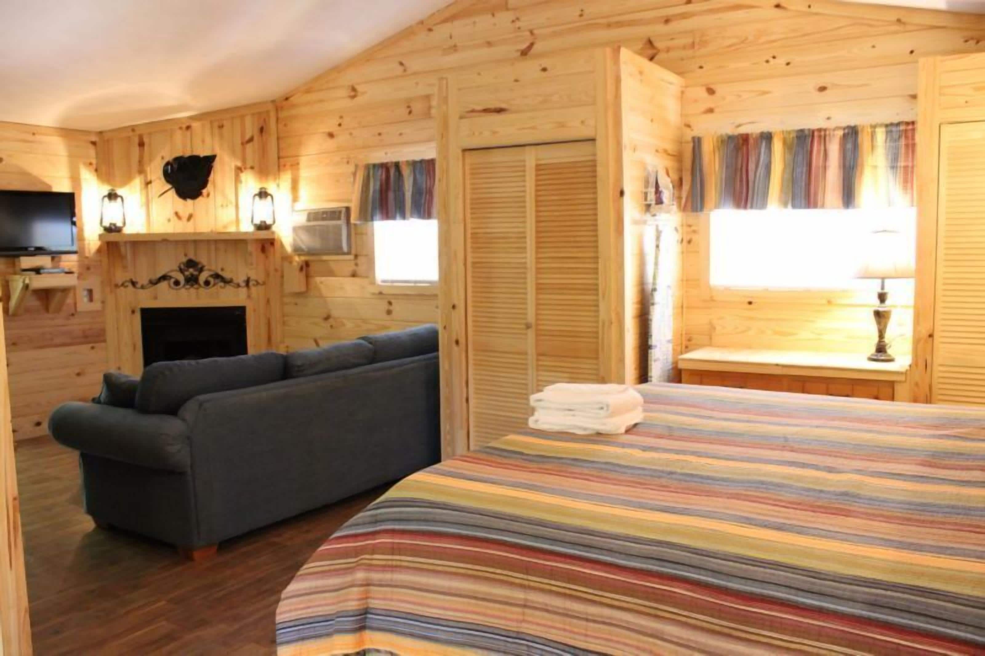 A cozy log cabin room with a sofa, a bed with a striped blanket, a fireplace, and a television.