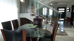 Ein moderner Essbereich mit Glastisch und Holzsesseln, einer Treppe und Blick ins Freie.