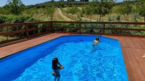 Una piscina rectangular con un deck de madera que la rodea, con un viñedo y colinas al fondo.
