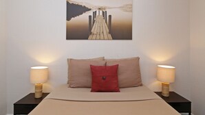 A bedroom with a bed, two bedside lamps, a red pillow, and a painting of a dock on a wall. - Refurbished.  Accessible. Step free access, disabled parking, walk in shower. (Kissimmee)