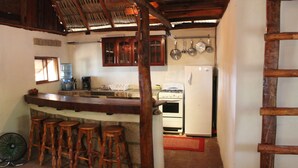 Una cocina con una barra de madera, taburetes, un refrigerador y ollas colgantes.