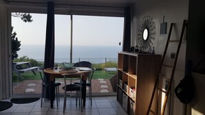 Habitació amb porta de vidre corredissa que dona a un pati amb vista al mar. A l'interior, hi ha una taula de fusta amb cadires i una estanteria.