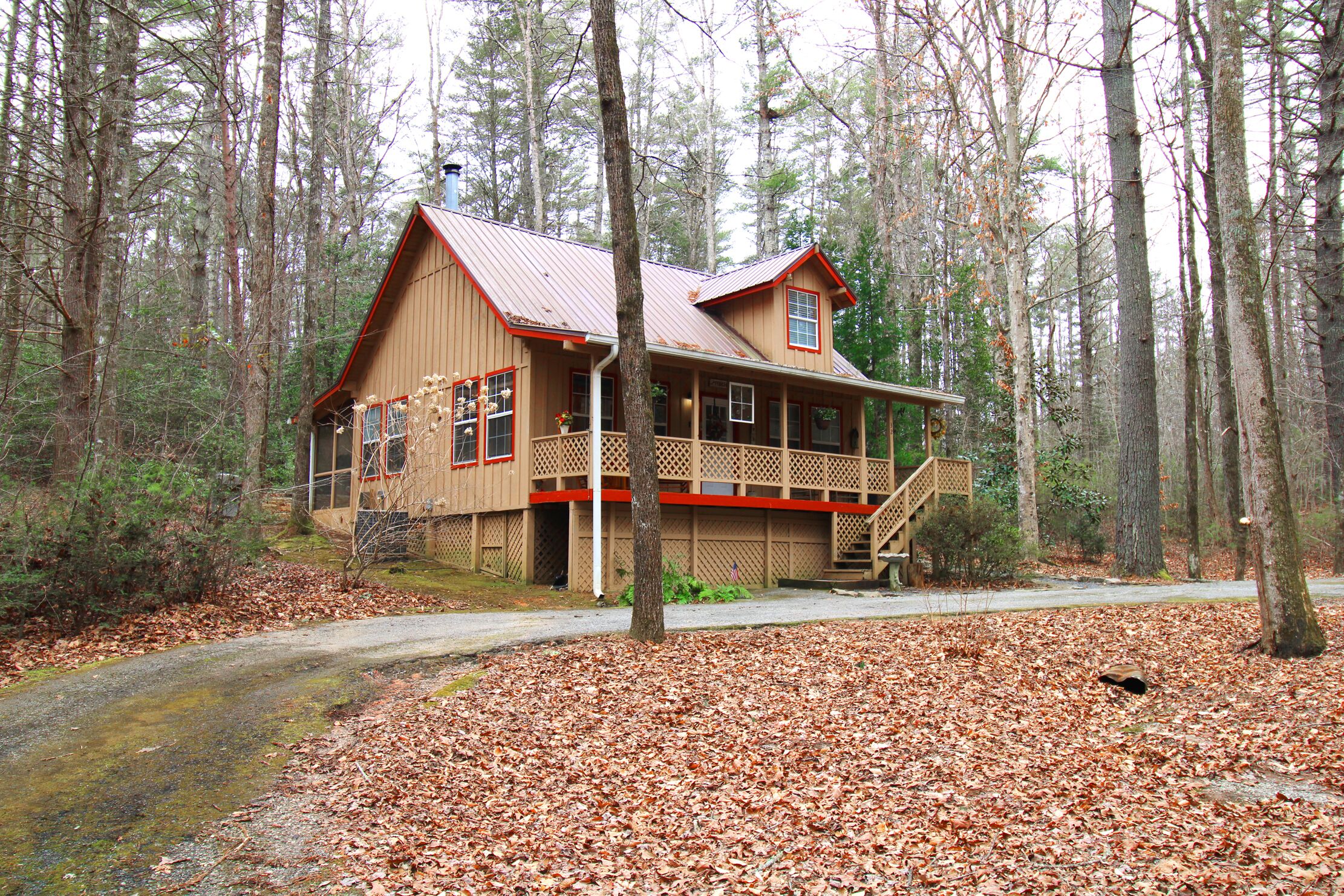 A wooden cabin with a porch and a chimney, surrounded by a forest.