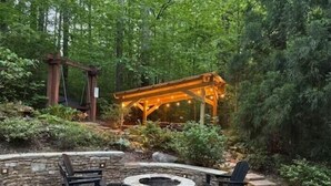 Pihalla on oleskelualue, jossa on nuotiopaikka, ulkokalusteita ja puinen pergola, jonka yllä on valoketju.