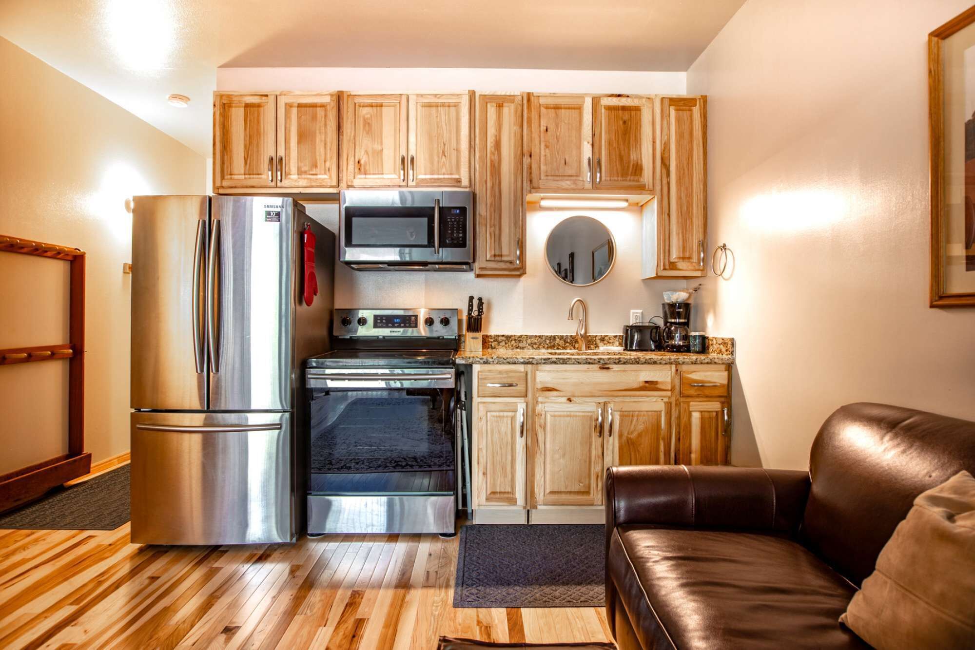 A compact kitchen with wooden cabinets, a stainless steel refrigerator, a microwave, an oven, and a coffee maker.