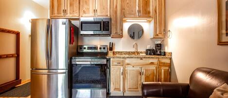 A compact kitchen with wooden cabinets, a stainless steel refrigerator, a microwave, an oven, and a coffee maker.