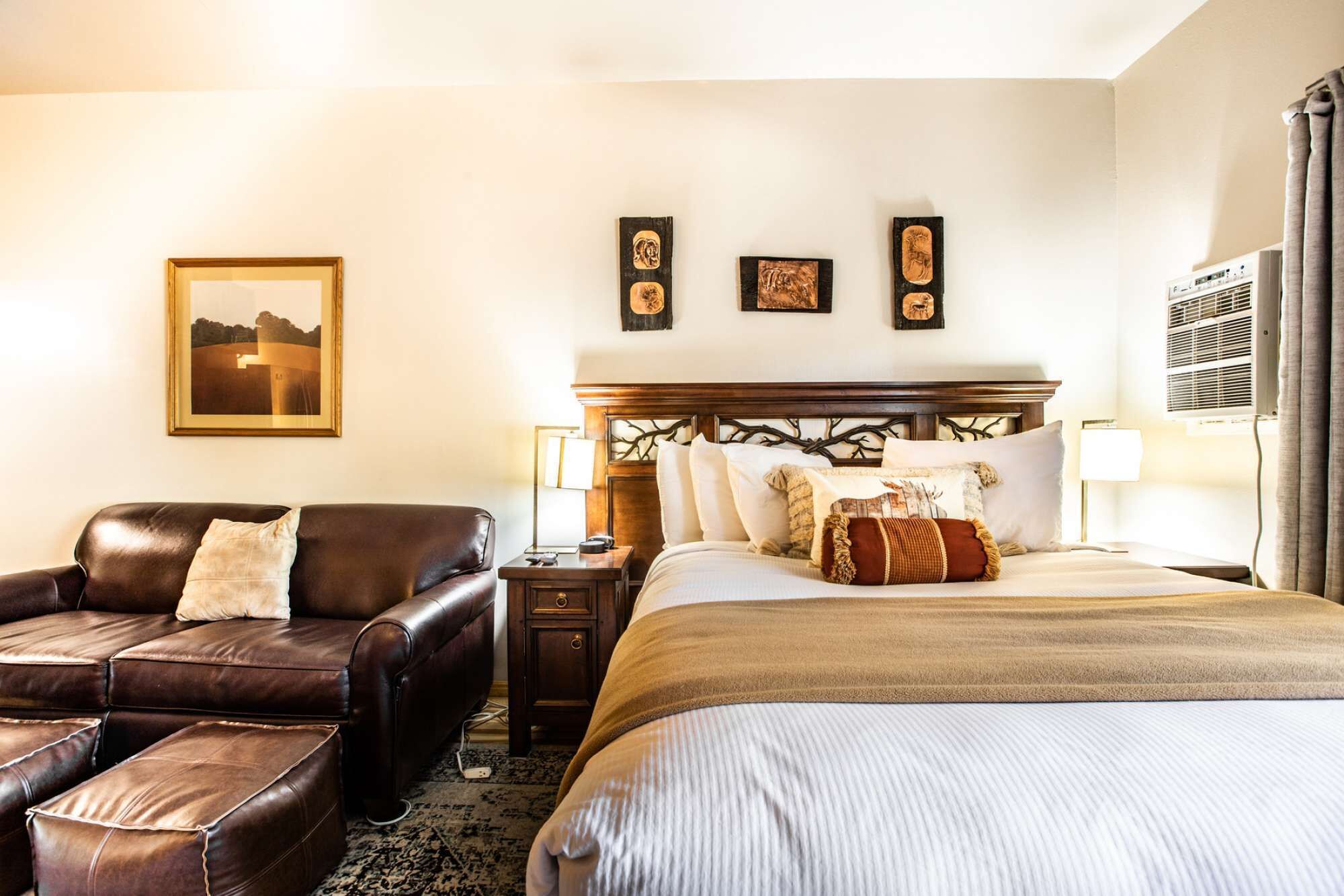 A hotel room with a bed, a leather sofa, a nightstand, and a wall-mounted air conditioning unit.