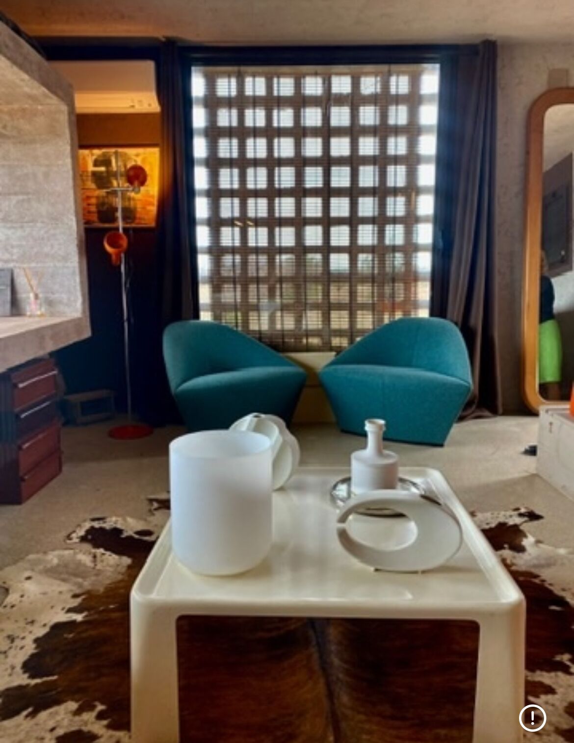 Una habitación con dos sillas color turquesa, una mesa de centro blanca y un tapiz de cuero de vaca.