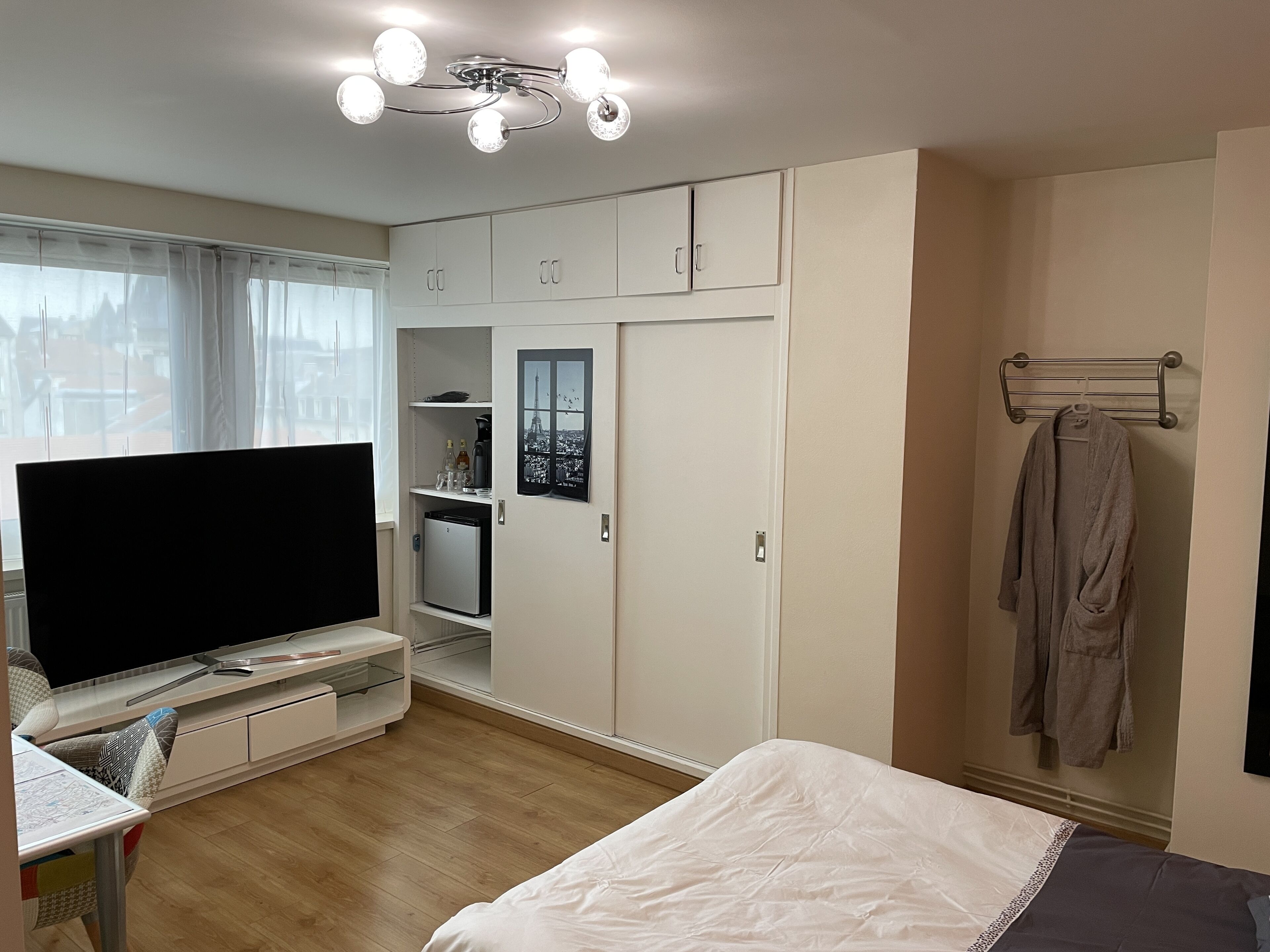 A bedroom with a bed, a TV, a wardrobe, and a small kitchenette.