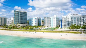 A beachfront hotel with multiple high-rise buildings, a sandy beach, and palm trees. - 2bd Bayfront Ste Bay View w/balcony, Pool, nearby dining, beach access (Miami Beach)