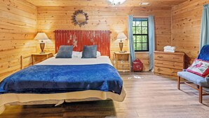 A wooden cabin bedroom with a bed, two bedside tables with lamps, a ceiling fan, a window with curtains, and a dresser. - Country Charm C - One of four Pet Friendly group cabins in Helen (Helen)