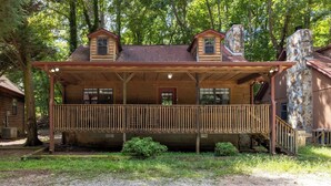 A wooden cabin with a covered porch, a stone chimney, and a gravel driveway. - Country Charm C - One of four Pet Friendly group cabins in Helen (Helen)