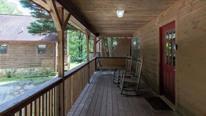 A wooden porch with a red door, a bench, and a view of a house and trees. - Country Charm C - One of four Pet Friendly group cabins in Helen (Helen)