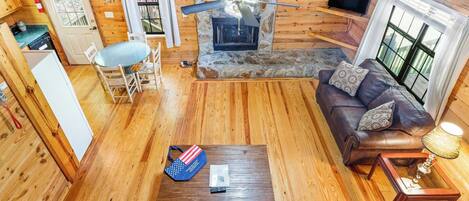 A cozy cabin interior with a stone fireplace, wooden floors, a leather sofa, and a dining area.