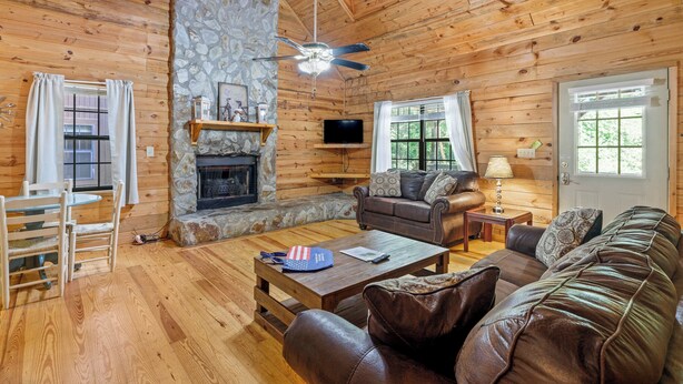 A cozy cabin interior with a stone fireplace, wooden walls, a leather sofa, and a television. - Country Charm C - One of four Pet Friendly group cabins in Helen (Helen)