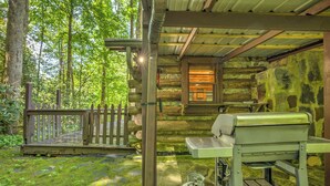 A rustic cabin with a wooden porch, a propane grill, and a stone wall. - Adanaylah - A True Log Cabin Experience. Pet Friendly, too! (Hiawassee)