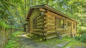 A rustic log cabin with a stone-paved entrance, surrounded by lush greenery. - Adanaylah - A True Log Cabin Experience. Pet Friendly, too! (Hiawassee)