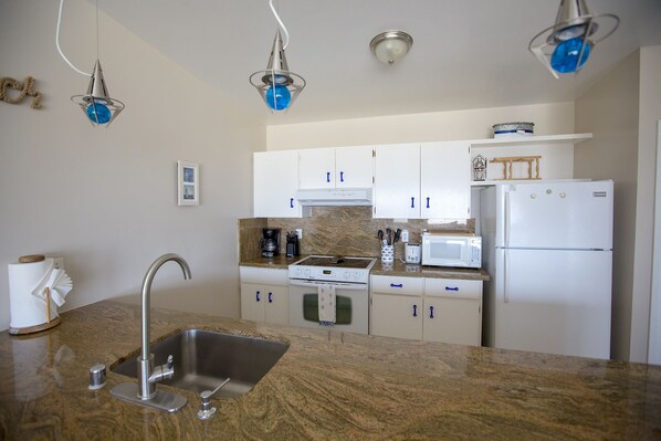 A modern kitchen with white cabinets, a stainless steel sink, a stove, a microwave, and a refrigerator.