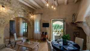Un interior rústico con paredes de piedra, vigas de madera, una zona de comedor con una mesa para cuatro, y un televisor fijado a la pared.