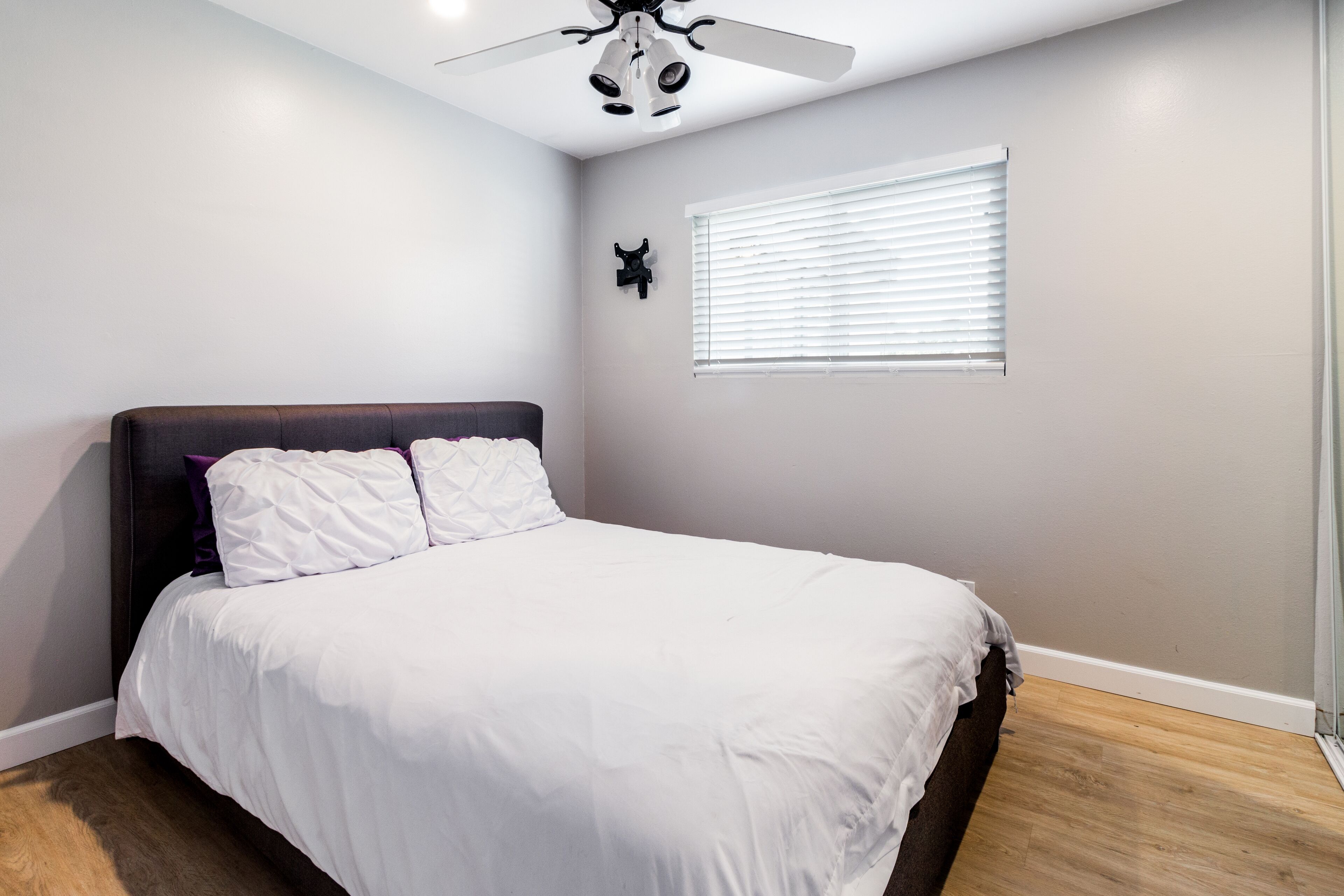 A bedroom with a bed, a ceiling fan, a window with blinds, and a wall-mounted decoration.